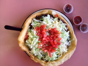 A Navajo taco is fry bread topped with Navajo chili, lettuce, cheese, tomato and salsa.